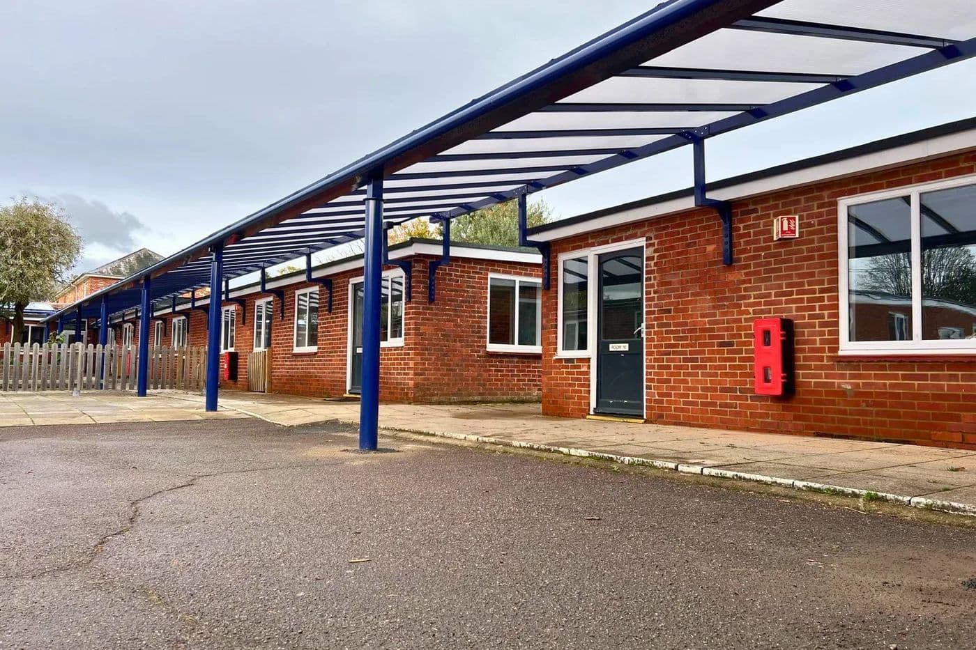 Blue aluminium covered walkway with a clear polycarbonate roof running along a single-storey school building