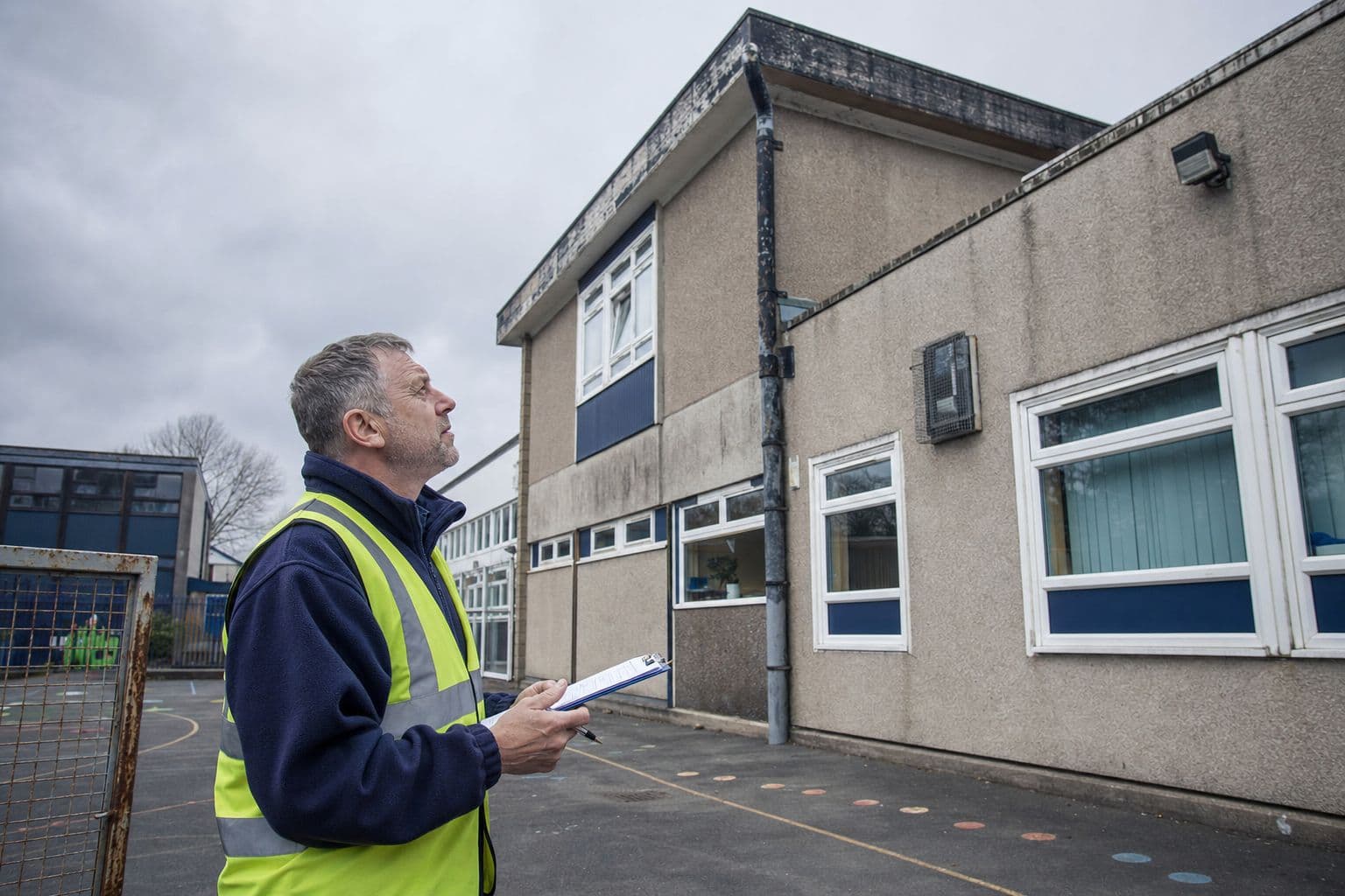 Surveyor in a hi-vis vest inspecting an older school building from the playground