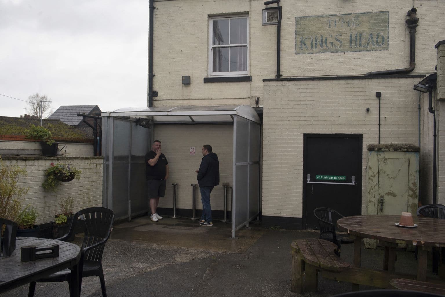 Pub beer garden with two people standing in an enclosed smoking shelter
