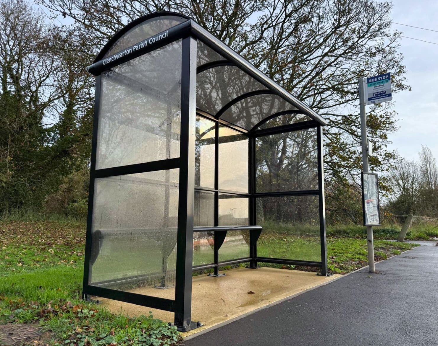 Black curved roof bus shelter with clear panels on a rural verge