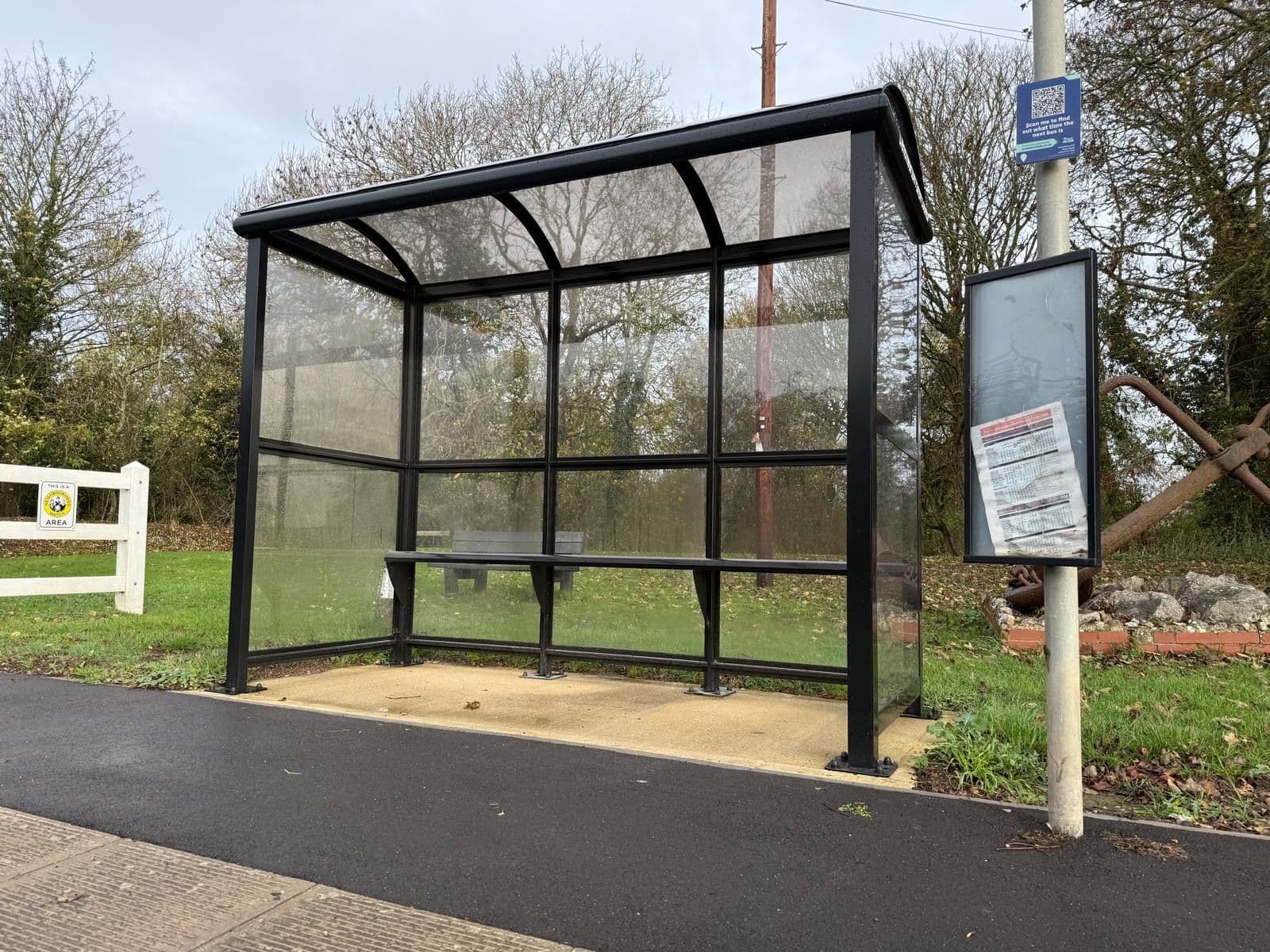 Black curved roof bus shelter with clear panels at a roadside stop