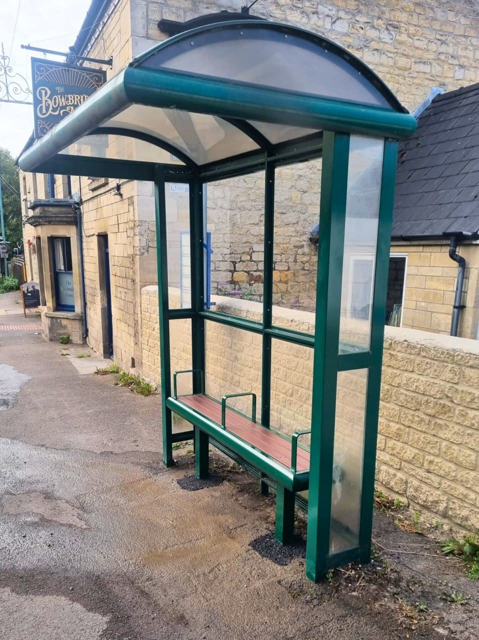 Refurbished green bus shelter with a curved roof on a Stroud street