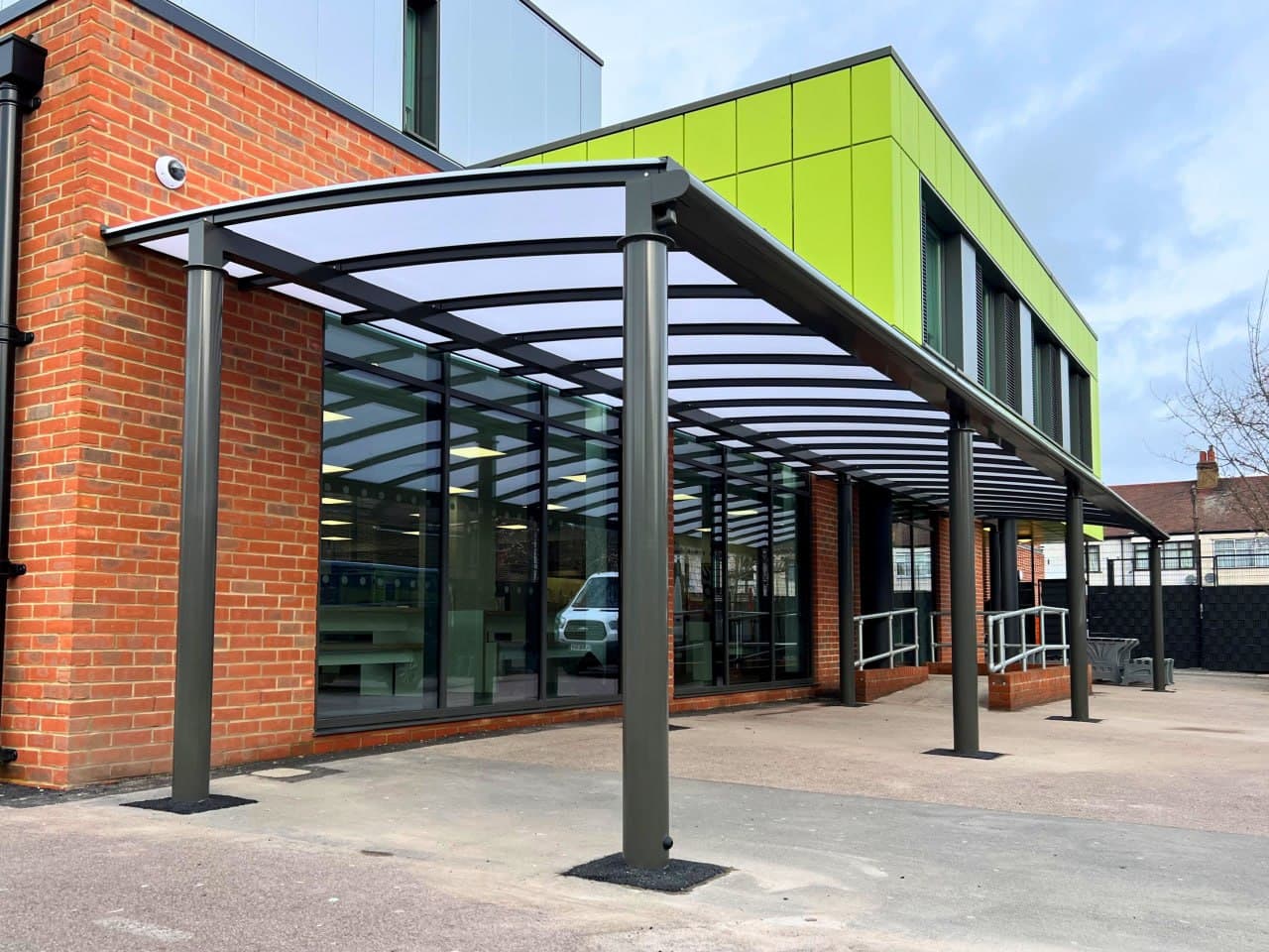 Anthracite bow roof walkway canopy at school entrance, curved polycarbonate roofing, modern school building with lime green cladding