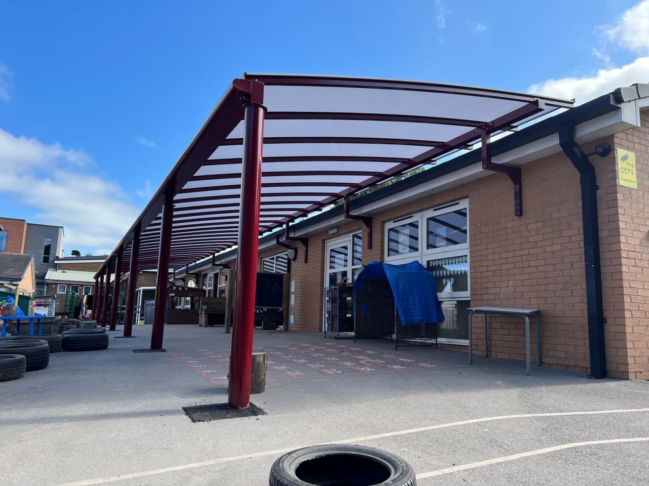Burgundy bow roof canopy at primary school, long-run polycarbonate roofing, playground installation