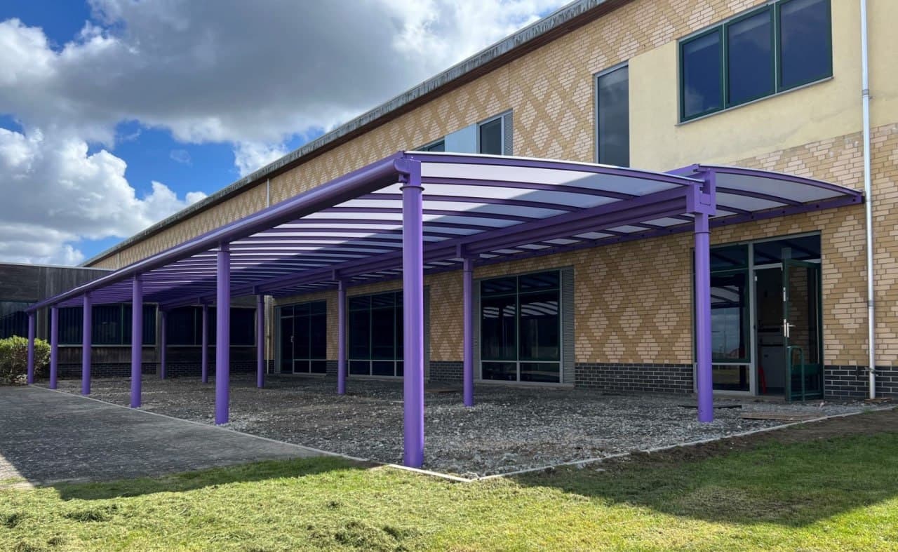 Purple bow roof canopy at school, curved polycarbonate roofing on purple aluminium frame, modern yellow brick school building