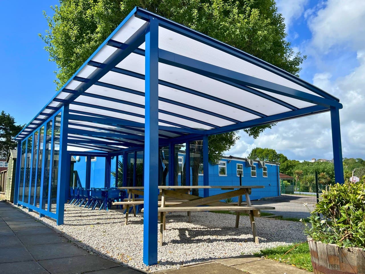 Blue semi-enclosed school canopy with polycarbonate side panels and bow roof, outdoor dining area, school installation