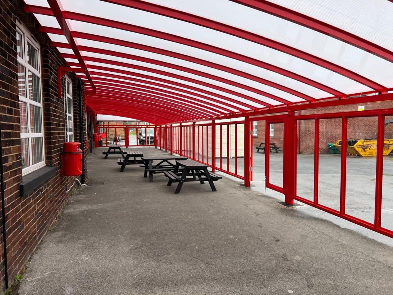 Enclosed covered walkway with red aluminium frame and polycarbonate side panels, school dining area underneath, long-run installation