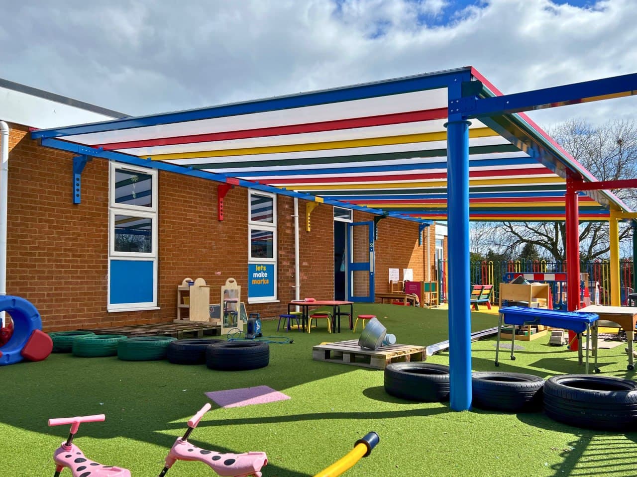 Multicoloured primary school canopy with blue, red, yellow and green aluminium frame, polycarbonate roof, outdoor learning area